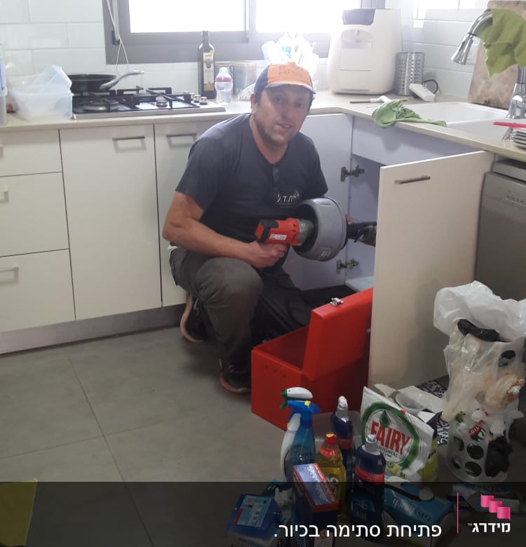 אינסטלטור עובד מתחת לכיור עם כלי עבודה